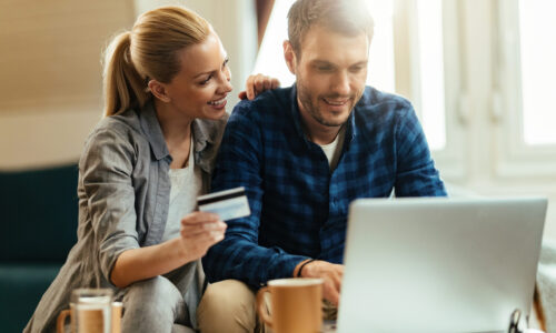Young happy couple home shopping while using computer and credit card.